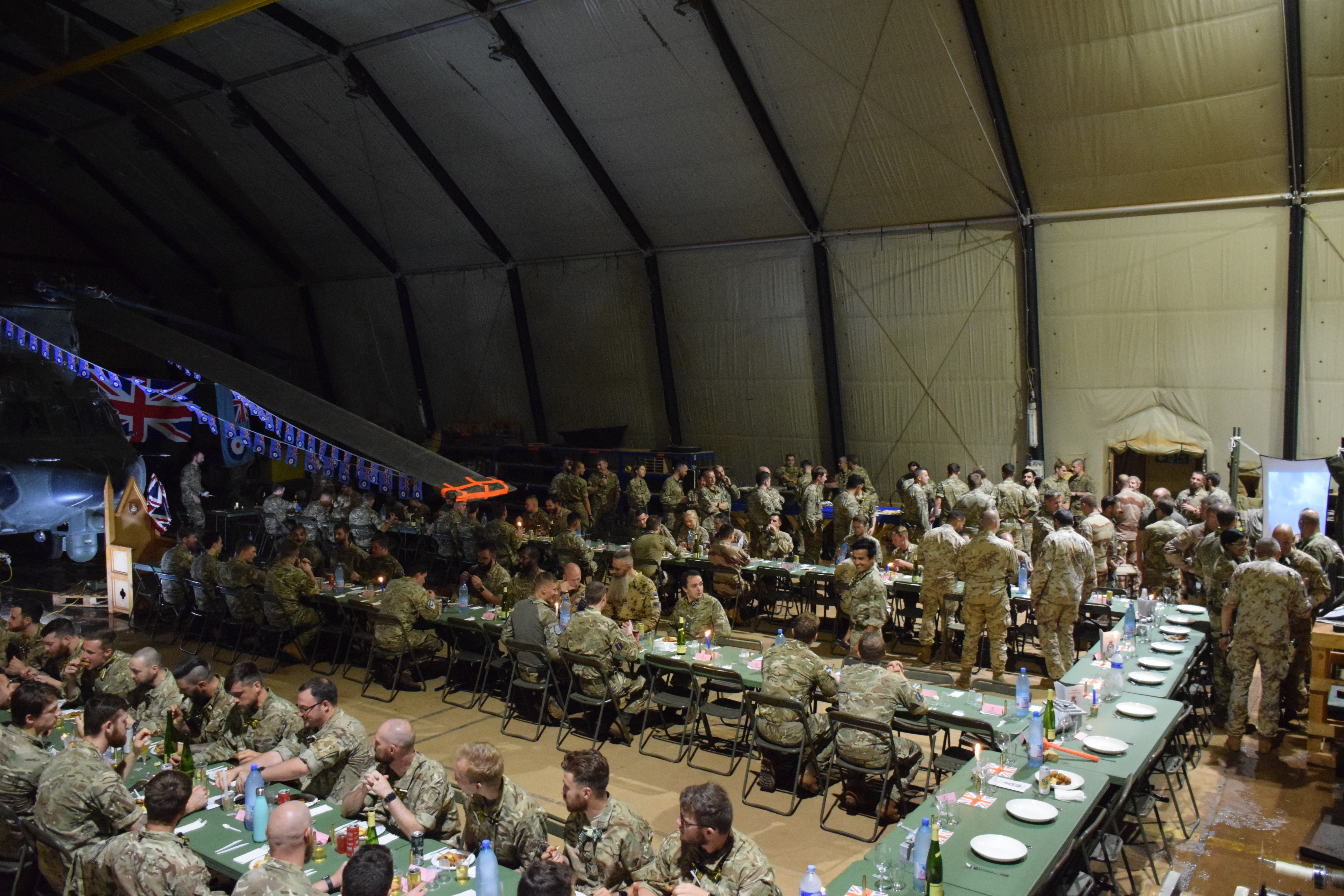 Personnel sit inside a hangar to eat. 